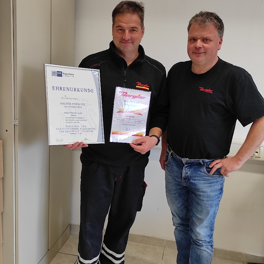 Zwei Herren, der Jubilar J. Pierschel links im Bild und Betriebsleiter aus Marktredwitz R. Schultes rechts, lächeln in die Kamera. In den Händen hält Hr. Pierschel eine Urkunde für seine Betriebstreue. 