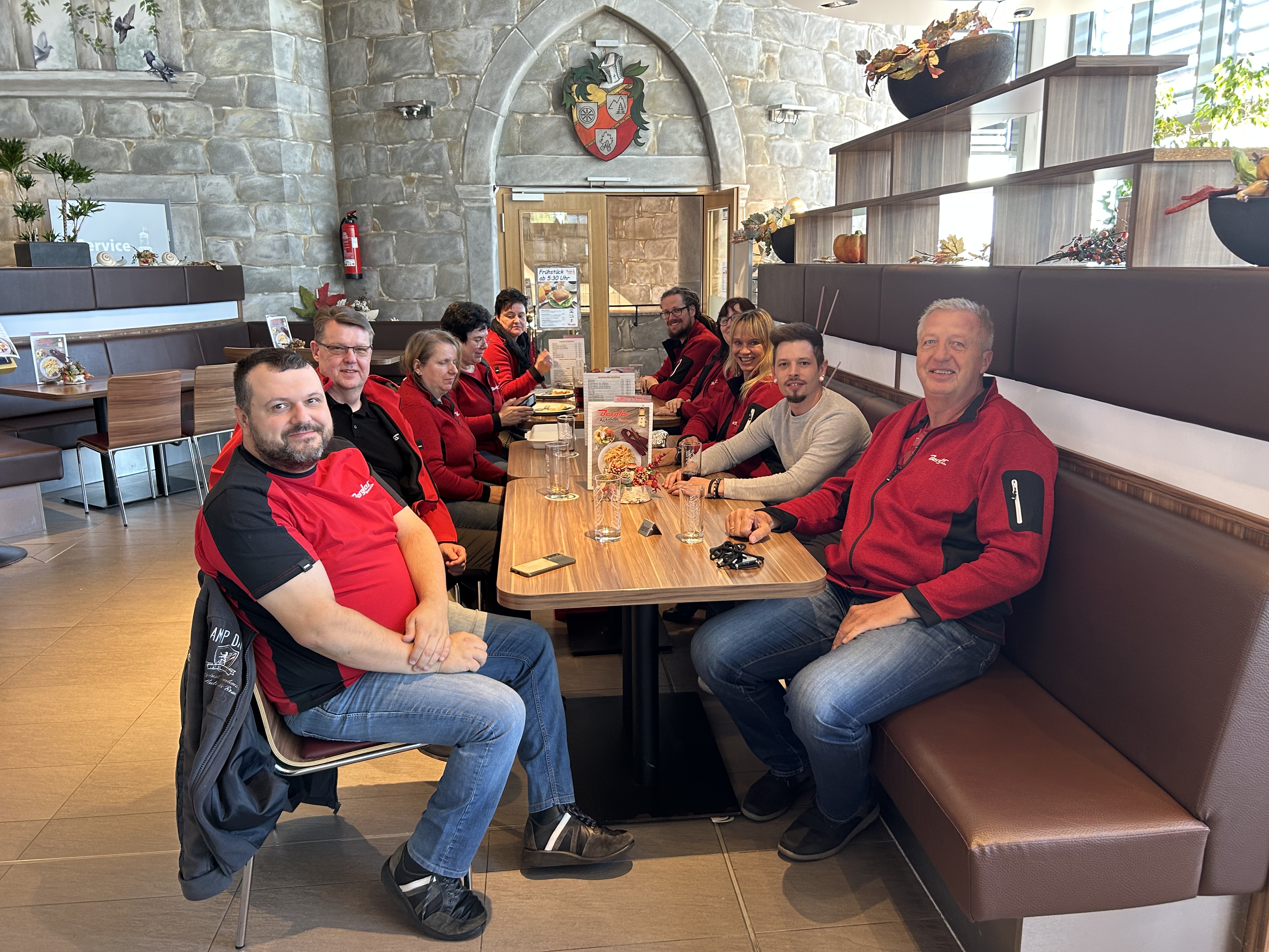 Unsere Kolleginnen und Kollegen mit roten Jacken sitzen am Esstisch am Autohof in Windischeschenbach und lachen in die Kamera.